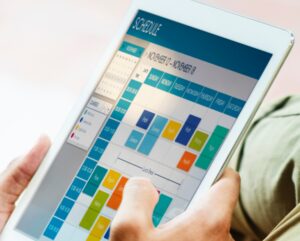A person holds a tablet displaying a colorful digital Social Media Calendar, featuring various events and appointments scheduled for the week of November 12 to November 18.