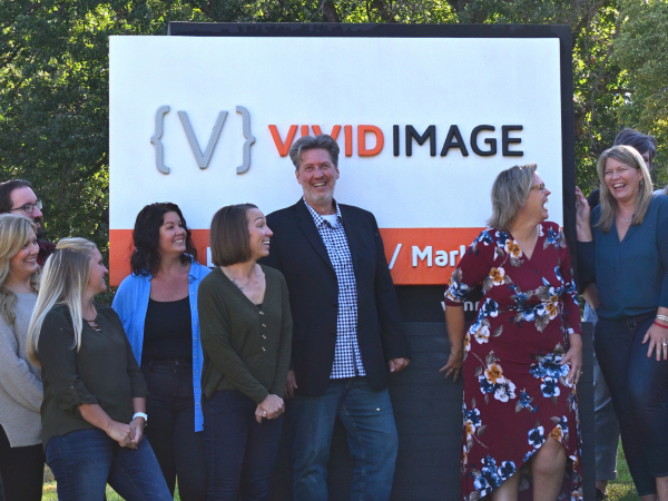 vivid image team smiling in front of signage
