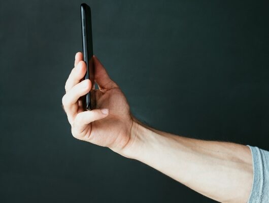 A person’s hand holding a black smartphone vertically in front of a dark, plain background, as if browsing a guide to content marketing.