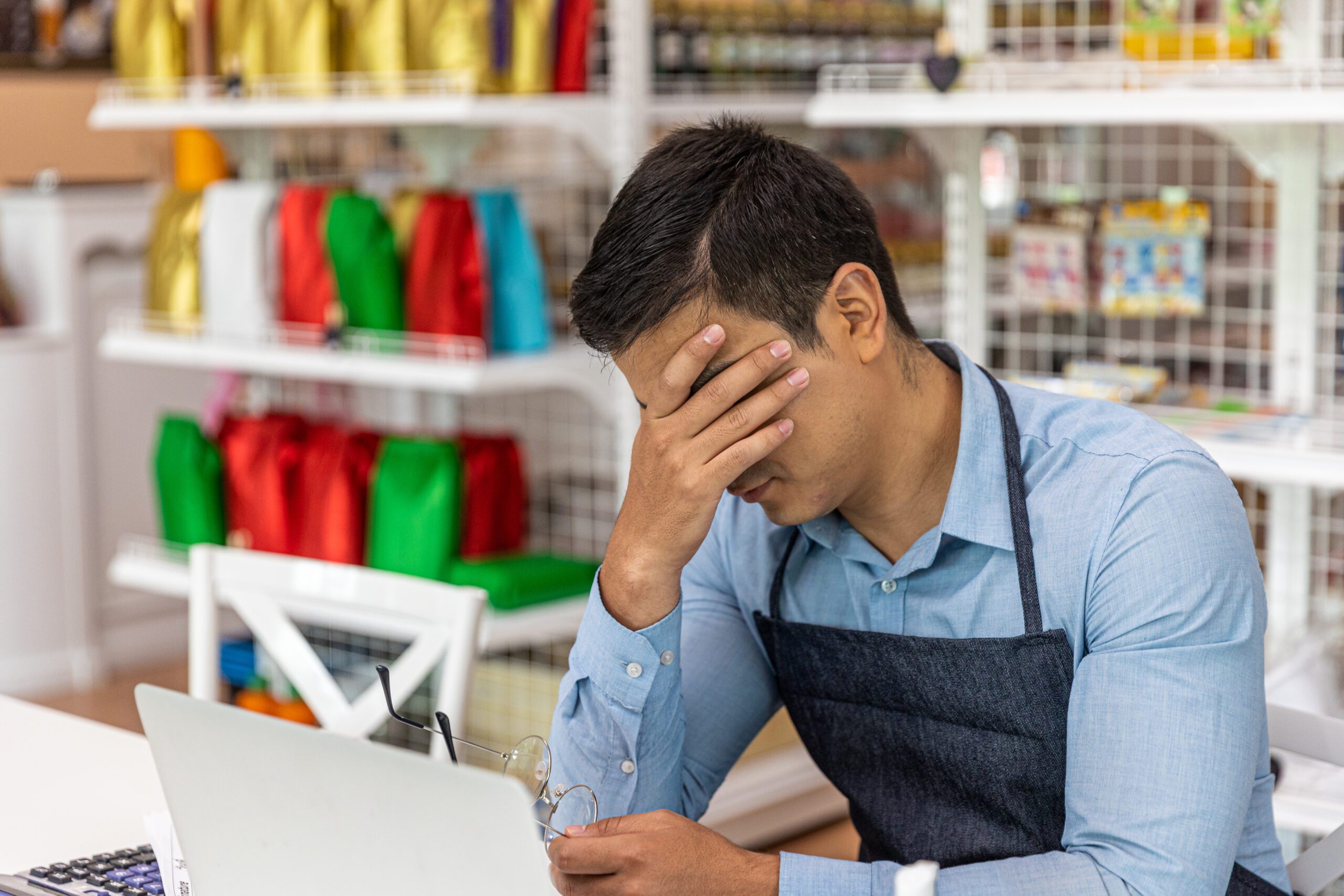 Young frustrated male store owner using computer at his small business.