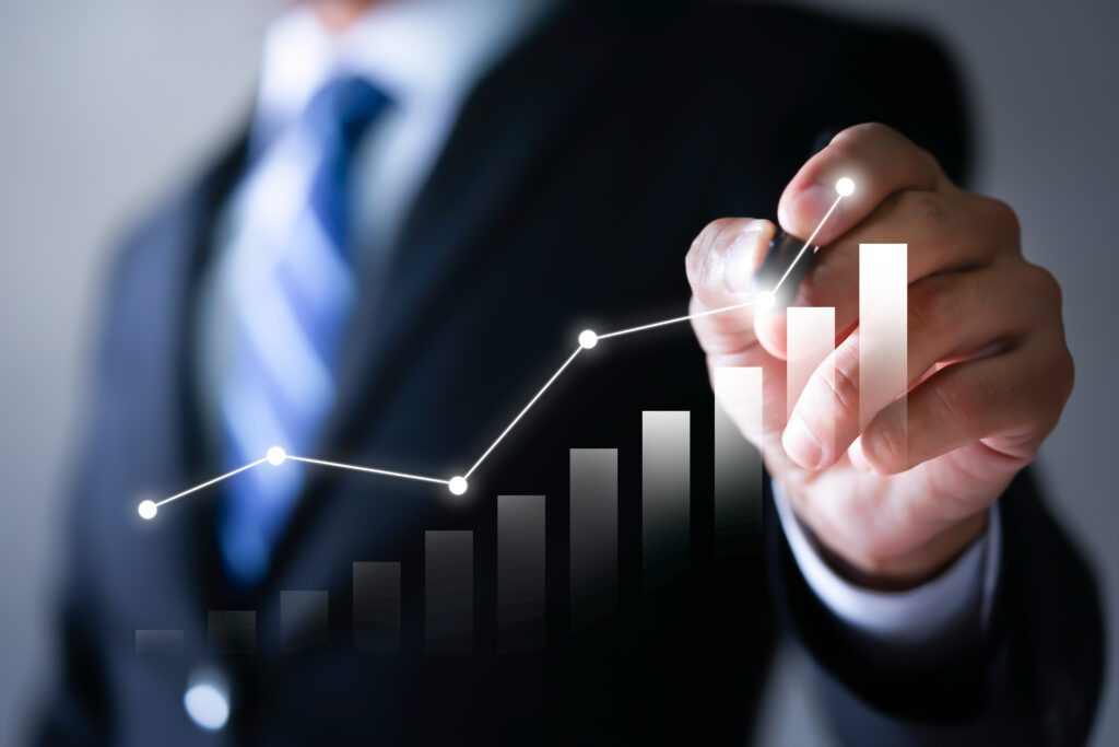 A person in a suit draws a rising line graph with a marker, illustrating growth or success—an ideal image for learning how to grow a referral-based business over a blurred bar chart background.