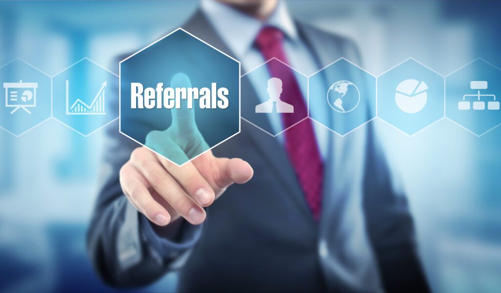A person in a suit touches a transparent screen featuring icons and the word Referrals highlighted in a hexagon, symbolizing business networking and referral systems.