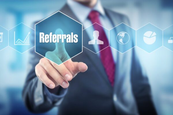 A person in a suit touches a transparent screen featuring icons and the word Referrals highlighted in a hexagon, symbolizing business networking and referral systems.