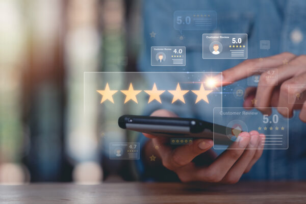 A person uses a smartphone, tapping a digital display with five gold stars, representing a high rating—demonstrating how to use Google reviews. Floating icons show customer reviews and ratings in the background.